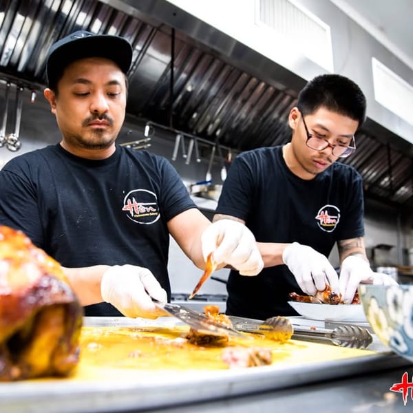 Two Hên Vietnamese Restaurant chefs in black shirts and gloves preparing food in a kitchen.