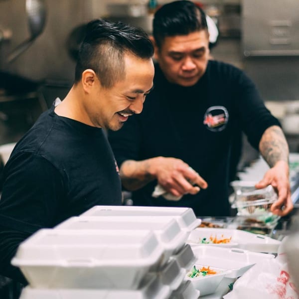 Two Hên Vietnamese Restaurant chefs preparing takeout orders in a busy kitchen.