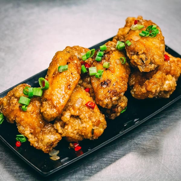 Crispy Vietnamese chicken wings on a black plate, garnished with green onions and red chilies.