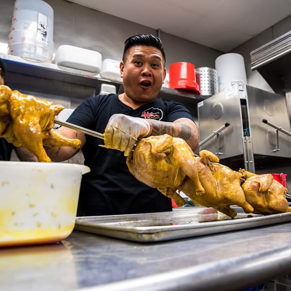 Chef in a commercial kitchen preparing whole chickens on rotisserie skewers for Hên Vietnamese Restaurant.